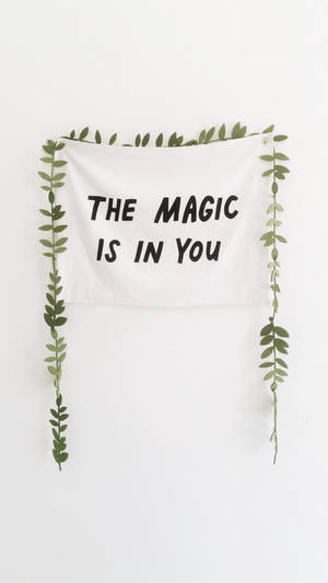 白色掛牆飾物，黑色文字寫著「The Magic Is In You」，由綠色藤蔓框住。