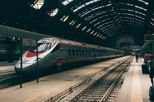 一列現代高速列車在歷史悠久的火車站，乘客在月台上等候。