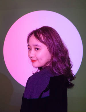 年輕女性在粉紅色圓形燈光前微笑。 — 淺粉紅色美學動圖 壁紙