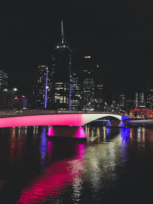 夜晚，一座燈光明亮的現代橋樑橫跨水面，背景是城市天際線。
