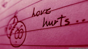 粉紅色間線紙上以手寫文字「love hurts」和塗鴉的悲傷臉孔。 — 夜空 壁紙