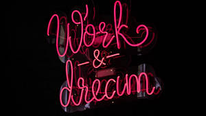 粉紅色霓虹燈牌，上面寫著 Work & Dream，置於深色反光表面。 — 淺粉紅色 壁紙
