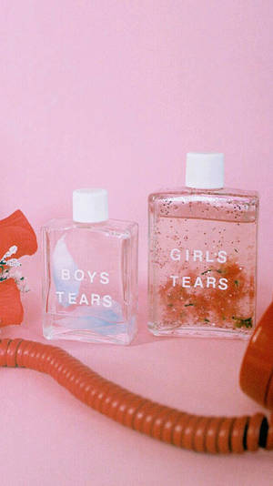 兩個香水瓶，標有 boys tears 和 girls tears，放在粉紅色背景上，配有一條橙色電話線。