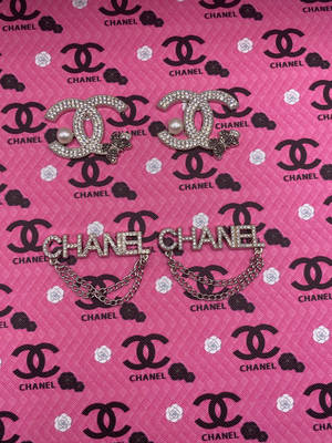 兩枚 Chanel 胸針，飾有珍珠和鏈條，放在品牌粉紅色布料上。