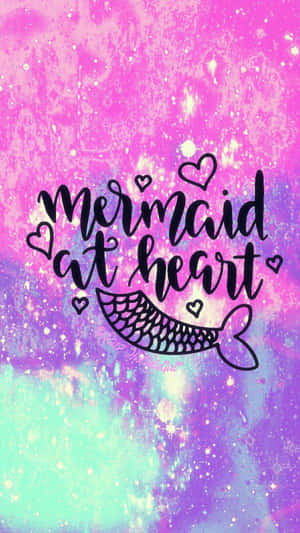 在色彩繽紛的宇宙背景上，帶有魚尾和心形的「mermaid at heart」文字。