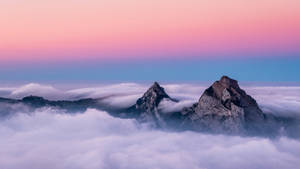 黎明時分，兩座山峰從雲層中浮現，天空呈現粉紅和藍色。