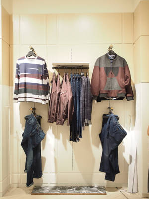 極簡主義服裝展示，在壁掛式架子和掛鉤上展示毛衣、夾克和牛仔褲。