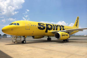 藍天白雲下，黃色Spirit Airlines飛機停在機場停機坪上。