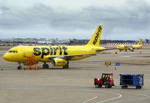 黃色Spirit Airlines飛機停在機場停機坪，附近有地勤服務車輛。