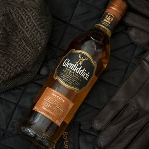 Glenfiddich 威士忌酒瓶與粗花呢帽和皮手套放在黑色外套上。