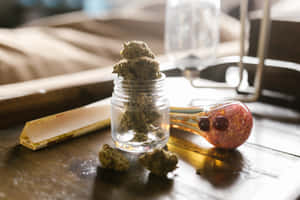 玻璃罐中的大麻花蕾、水煙槍和捲煙紙在木桌上。 — 食草 壁紙