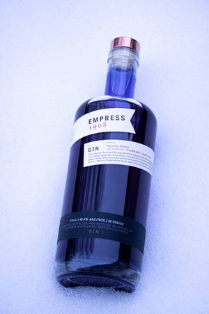 一瓶標有Empress 1908的深藍色氈酒瓶，在藍光下放置在雪地上。