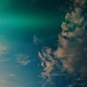青綠色和藍色的天空，雲朵被綠色極光照亮。