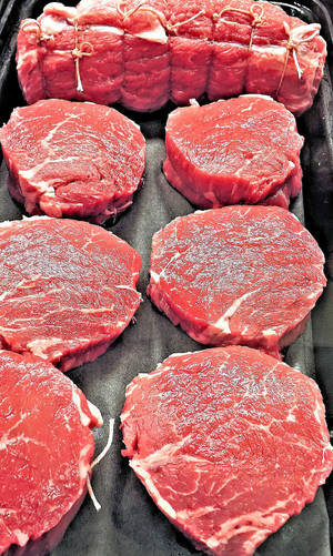 新鮮生牛肉扒和紮好的烤肉放在黑色托盤上。