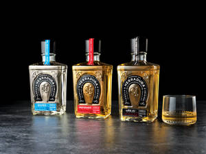 三瓶 Herradura 龍舌蘭酒和一杯龍舌蘭酒在深色表面上。