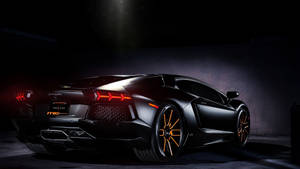在漆黑攝影棚中，配以橙色輪圈和紅色尾燈的黑色林寶堅尼 Aventador。