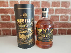 Aberfeldy 12年威士忌酒瓶和禮盒，白色表面配紅磚牆背景。