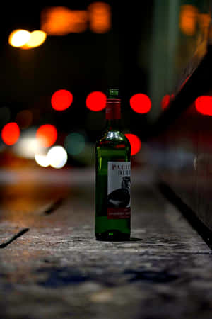 夜晚潮濕城市行人路上的一個綠色酒瓶，帶有模糊的車燈。 — Vivo Pad 壁紙