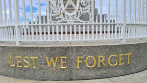 白色籬笆後方刻有金色銘文「Lest We Forget」的戰爭紀念碑。