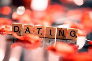 拼出 dating 的 Scrabble 拼字塊，在反光表面上被紅色玫瑰花瓣環繞。