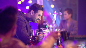 男子在紫色燈光下於酒吧微笑，背景有模糊的顧客和發光的球體。