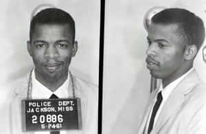 一名身穿西裝的男子大頭照，附有 Jackson Mississippi 警方登記標誌。 — 黑白 壁紙