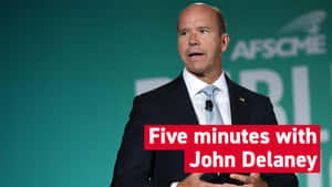 穿西裝的男子在活動中發言，橫幅寫着 'Five minutes with John Delaney'。 — 政治 壁紙