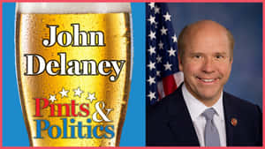 John Delaney 身穿西裝微笑站在美國國旗旁，帶有寫著 Pints & Politics 的啤酒杯圖案