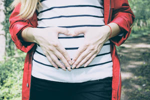 孕婦在森林中用雙手在肚子上方形成心形