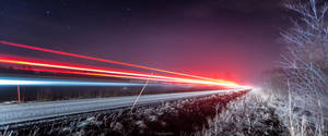夜晚結冰的路邊，星空下汽車燈光形成的光條。