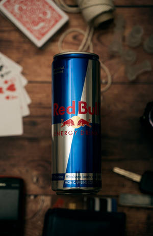 Red Bull罐裝飲品放在木桌上，旁邊有撲克牌、鑰匙和相機