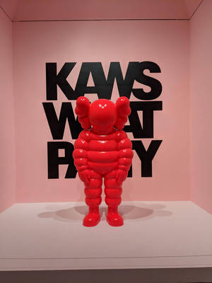 紅色KAWS Companion雕塑在粉紅色畫廊中展示，牆上有黑色文字。