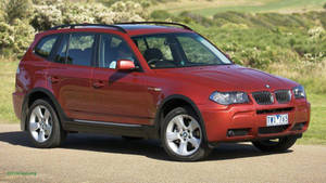 紅色BMW X3 SUV停泊在碎石路上，背景有翠綠山丘和灌木叢。 — 酷車 壁紙