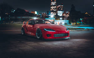 紅色跑車夜間停放，背景有城市燈光