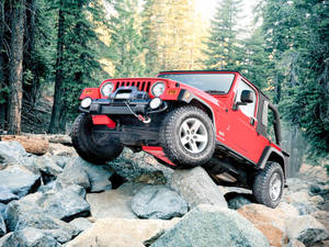 紅色Jeep Wrangler在森林中攀爬大岩石。