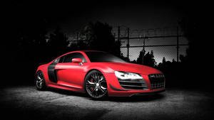 夜間在鐵絲網圍欄後方照亮的紅色奧迪R8跑車。 — Audi R8 GIF 壁紙