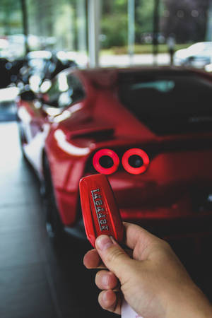 手在展廳內紅色跑車前拿著紅色法拉利鑰匙扣。 — 汽車 壁紙