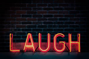 一個紅色霓虹燈牌，拼寫著 LAUGH，放在一塊木板上，靠著磚牆。