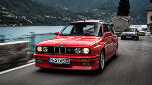 紅色BMW M3在風景如畫的湖邊道路上疾馳，帶有動態模糊效果。