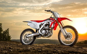 金色日落中泥坡上的紅白色本田 CRF 越野電單車。