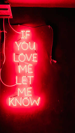 紅色霓虹燈牌，訊息為 'If you love me let me know'，置於深色牆上。