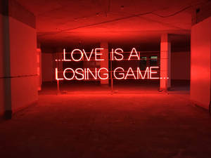 紅色霓虹燈牌，上面寫著「LOVE IS A LOSING GAME」，在一個空的混凝土空間中。 — 霓虹 壁紙