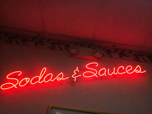 在復古餐廳環境中，一個寫著 Sodas & Sauces 的紅色霓虹燈牌。 — 霓虹 壁紙