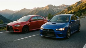 兩輛紅色和藍色的三菱Lancer Evolution汽車在日落時分行駛在山路上