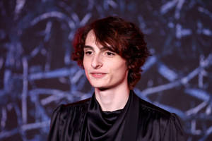身穿黑色緞面長袍的年輕男子在抽象藍色背景前對著鏡頭微笑。