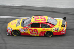 黃色和紅色的 NASCAR 賽車在賽道上疾馳，帶有動態模糊效果。