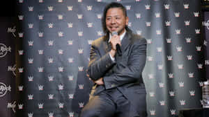 WWE活動中，身穿灰色西裝的摔角手微笑著手持麥克風。 — WWE GIF 壁紙