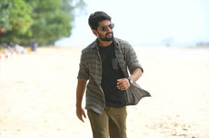 戴太陽眼鏡的男子在陽光明媚的海灘上行走，穿著格仔襯衫和卡其褲。
