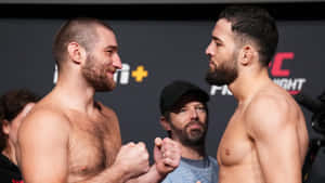 兩名赤裸上身的MMA拳手在緊張的賽前對視中鎖定拳頭。