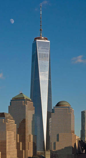 One World Trade Center摩天大樓，藍天中有月亮，周圍建築物沐浴在金色陽光中。